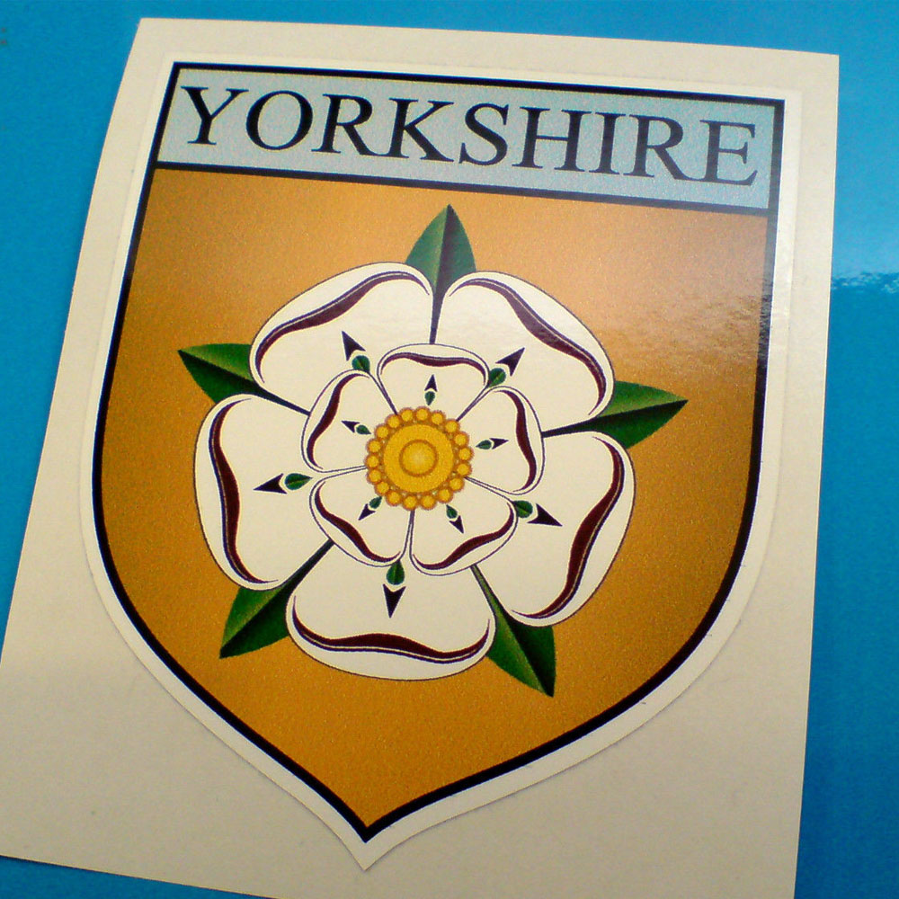 Yorkshire in black lettering on a blue banner across the top of a gold shield. Below is a white rose with a yellow centre and five green sepals.