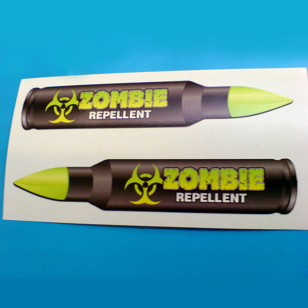 ZOMBIE REPELLENT STICKERS. A biohazard symbol and Zombie in fluorescent green lettering; Repellent in white lettering on a black bullet with a fluorescent green tip.