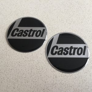 CASTROL STICKERS DOMED RESIN GEL. Castrol in black lowercase lettering on a silver L shaped background. Chrome edged. Black background.