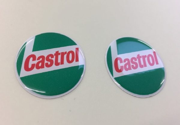 Circular sticker in red, white and green. Castrol bold red lowercase lettering on a white L shaped background. White edge. Green background.