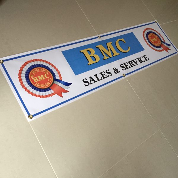 BMC SALES AND SERVICE BANNER. On the left and right sides are the red, white and blue BMC rosettes. Centre BMC gold bold lettering on a blue background. Below Sales and Service in black capital letters. White banner with blue edging.
