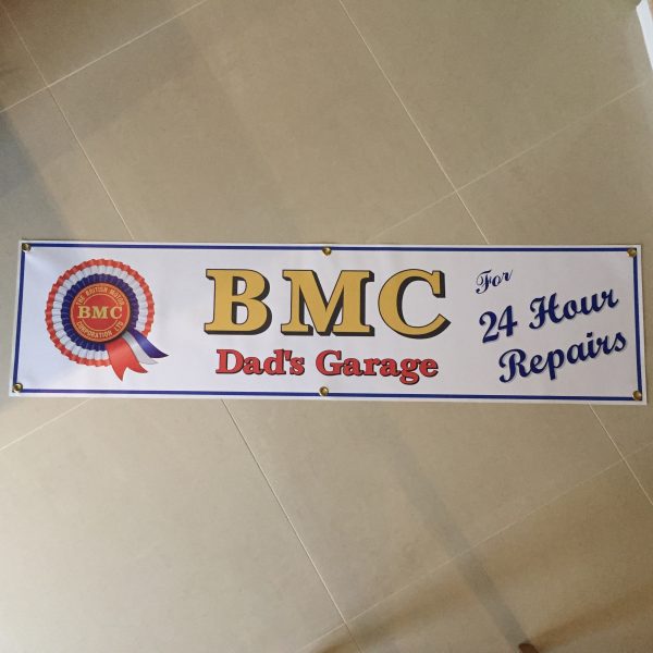 BMC 24 HOUR REPAIRS BANNER. On the left is the red, white and blue BMC rosette. Centre is BMC bold gold lettering. Dad's Garage lettering in red below. Right in blue lettering is For 24 Hour Repairs. White banner with blue edging.