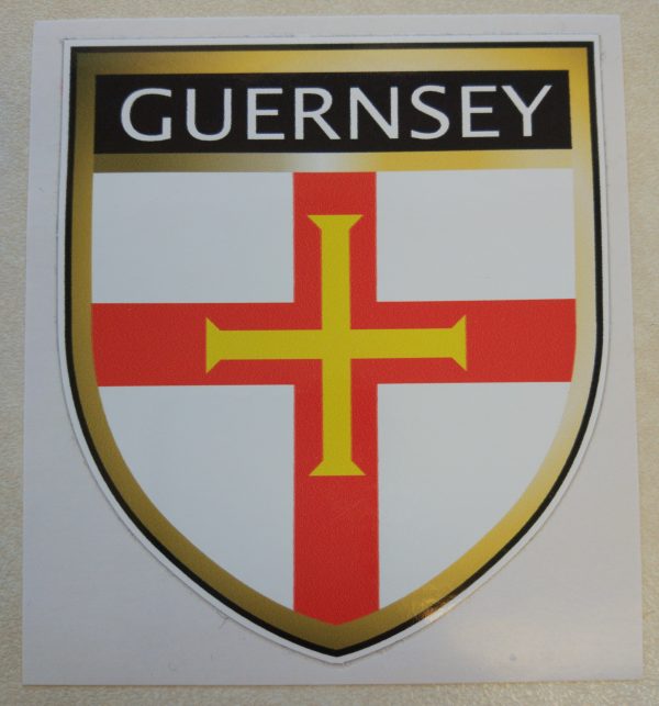 GUERNSEY FLAG SHIELD STICKER. Guernsey in white lettering on a black banner at the top of the shield. Below is a red cross with a gold cross within it on a white field.