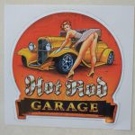 HOT ROD GARAGE STICKER. Hot Rod in white Gothic text, Garage in orange text on a black banner. A retro pin up in heels and a short dress leans over an orange hot rod with her gloved hands leaning on the wheel arch.