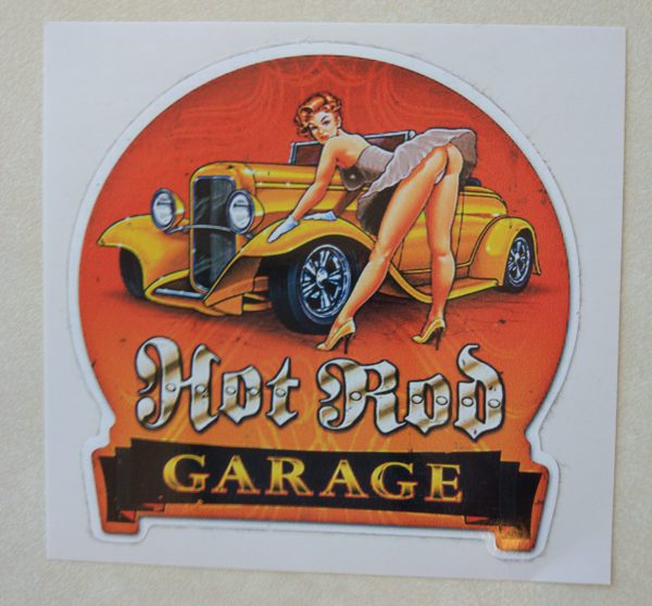 Hot Rod in white Gothic text, Garage in orange text on a black banner. A retro pin up in heels and a short dress leans over an orange hot rod with her gloved hands leaning on the wheel arch.