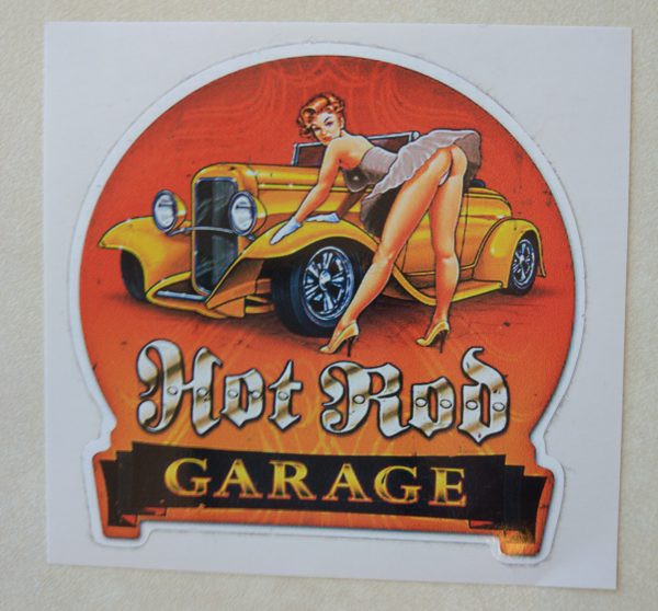 HOT ROD GARAGE STICKER. Hot Rod in white Gothic text, Garage in orange text on a black banner. A retro pin up in heels and a short dress leans over an orange hot rod with her gloved hands leaning on the wheel arch.