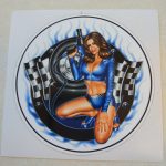 CHEQUERED 007 MODEL STICKER. A model with long dark hair wearing a skimpy blue and chequer top and shorts. She is kneeling in front of car tyres and black and white chequered flags. She is holding a wheel gun.
