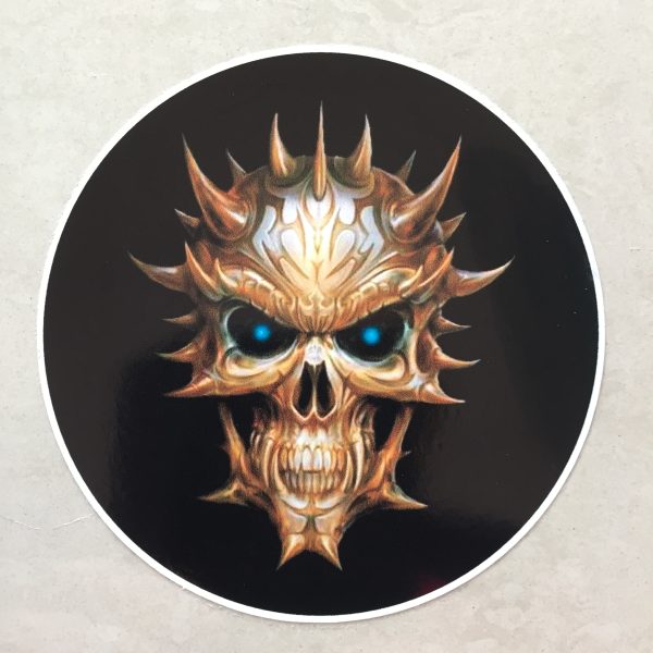 SKULL STICKER. A multi horned skull in hues of brown and white with piercing vibrant blue eyes and sharp teeth. A circular sticker with a black background.