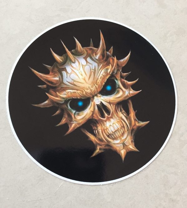 SKULL STICKER. A multi horned skull in hues of brown and white with piercing vibrant blue eyes and sharp teeth. A circular sticker with a black background.