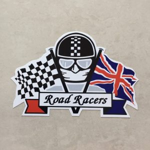 CHEQUERED ROAD RACERS STICKER. Road Racers in black lettering on a white banner. Behind are crossed chequered and Union Jack flags. The face of a motorcyclist wearing helmet, goggles and scarf sits between.