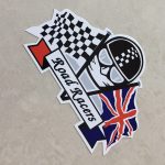 CHEQUERED UNION JACK ROAD RACERS STICKER. Road Racers in black lettering on a white banner. Behind are crossed chequered and Union Jack flags. The face of a motorcyclist wearing helmet, goggles and scarf sits between.