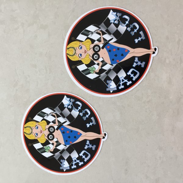 LADY LUCK STICKERS. Lady Luck in silver lettering on a black background. A blonde pin up wearing a number 8 bikini top and four aces sarong with a horseshoe in her hair. She stands in front of crossed chequered flags while holding a tool and a clover leaf.