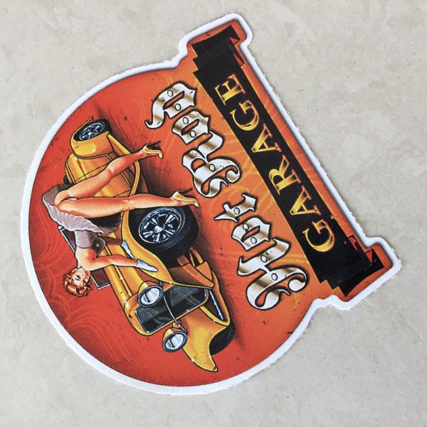 HOT ROD GARAGE STICKER. Hot Rod in white Gothic text, Garage in orange text on a black banner. A retro pin up in heels and a short dress leans over an orange hot rod with her gloved hands leaning on the wheel arch.