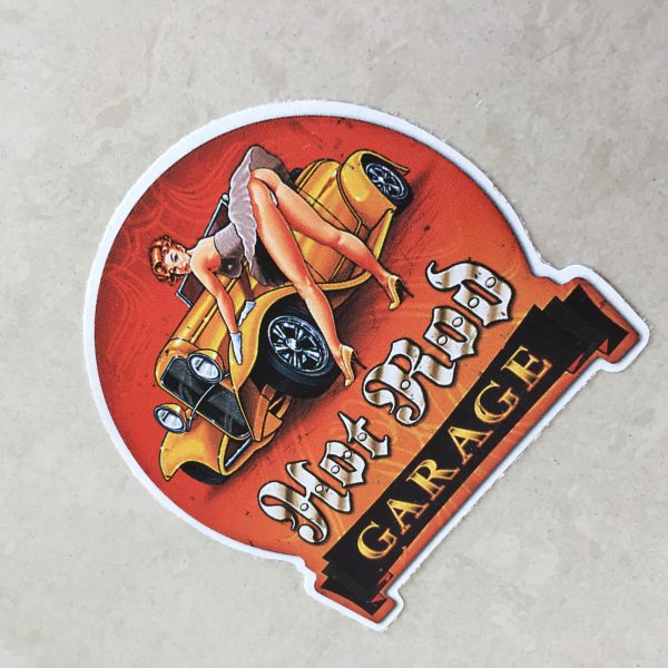 HOT ROD GARAGE STICKER. Hot Rod in white Gothic text, Garage in orange text on a black banner. A retro pin up in heels and a short dress leans over an orange hot rod with her gloved hands leaning on the wheel arch.