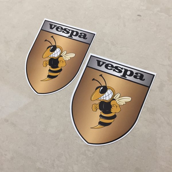 VESPA GOLD STICKERS. Vespa in black lettering on a silver banner at the top of the gold shield. A wasp displaying antennae, wings and white teeth is clenching its fists.