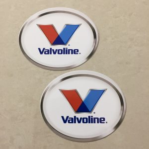 VALVOLINE LOGO STICKERS. Valvoline in blue lowercase lettering sits below a letter V in red and blue. An oval sticker with a white background and a chrome effect edge.