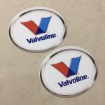 VALVOLINE LOGO STICKERS. Valvoline in blue lowercase lettering sits below a letter V in red and blue. An oval sticker with a white background and a chrome effect edge.