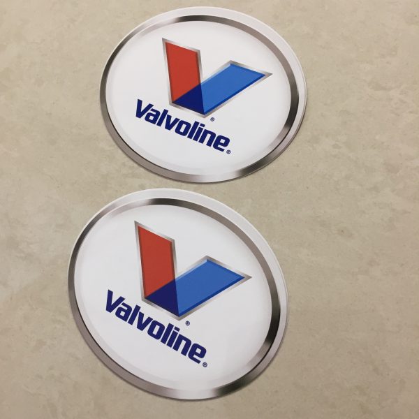 VALVOLINE LOGO STICKERS. Valvoline in blue lowercase lettering sits below a letter V in red and blue. An oval sticker with a white background and a chrome effect edge.