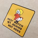 Hey! Watch My Behind Not Hers in black uppercase lettering on a yellow square sticker. A humorous female with yellow hair wearing a red dress and stockings is in the centre. She has her hand to her mouth while showing her behind.