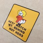 WATCH MY BEHIND STICKER. Hey! Watch My Behind Not Hers in black uppercase lettering on a yellow square sticker. A humorous female with yellow hair wearing a red dress and stockings is in the centre. She has her hand to her mouth while showing her behind.