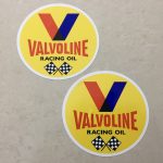 Valvoline in red and Racing Oil in black uppercase lettering. Above is the letter V in red and blue. Below are two crossed chequered flags on a yellow circular sticker.Valvoline in red and Racing Oil in black uppercase lettering. Above is the letter V in red and blue. Below are two crossed chequered flags on a yellow circular sticker.