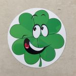 LUCKY CLOVERLEAF STICKER. A humorous sticker. A green cloverleaf with happy eyes and a broad smile. The mouth is open displaying white teeth and a red tongue.