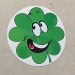 A humorous sticker. A green cloverleaf with happy eyes and a broad smile. The mouth is open displaying white teeth and a red tongue.