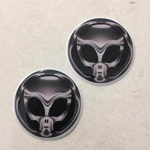 SKULL GEAR STICK STICKERS. A grey/chrome effect domed circular sticker. A skull with large black eye sockets on a black background.