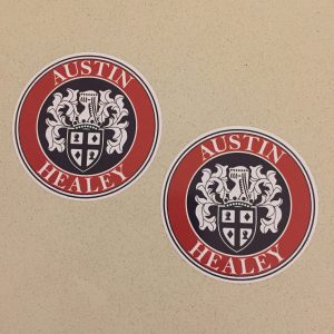 AUSTIN HEALEY STICKERS. Austin Healey in white lettering surrounds a brown circular sticker. In the centre on a black background is the Austin-Healey shield logo.