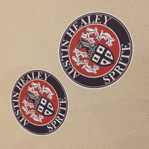 AUSTIN HEALEY SPRITE STICKERS. Austin Healey Sprite in white lettering surrounds a black circular sticker. In the centre on a brown background is the Austin-Healey shield logo.