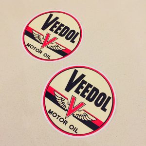 Veedol Motor Oil in black lettering on a circular sticker. The letter V in red overlays a pair of wings and two horizontal bands in red and black.