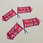 MILLE MIGLIA 1000 FLAG STICKERS. Two crossed flags. 1000 Miglia in white lettering on a red direction of travel arrow with a white border.