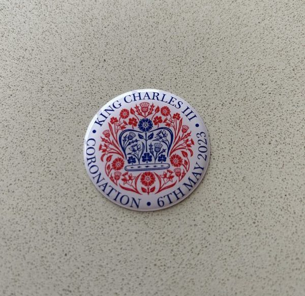 KING CHARLES CORONATION DOMED RESIN GEL STICKER. King Charles lll Coronation 6th May 2023 in blue lettering surrounds this white domed sticker. In the centre is a blue crown made up of roses, thistles, daffodils and shamrocks. These flowers, in red, surround the crown.